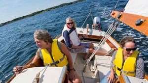 Three people on a sailboat wearing life vests
