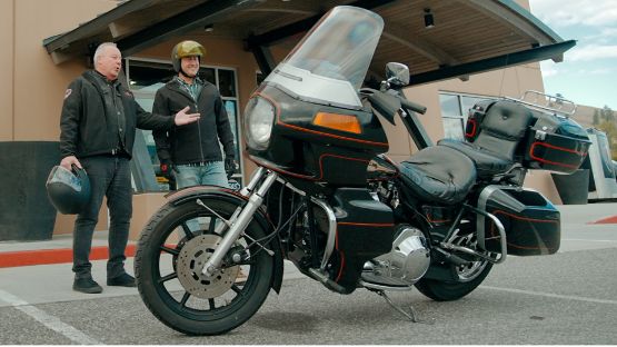 Two men standing beside a black Harley Davidson motorcycle